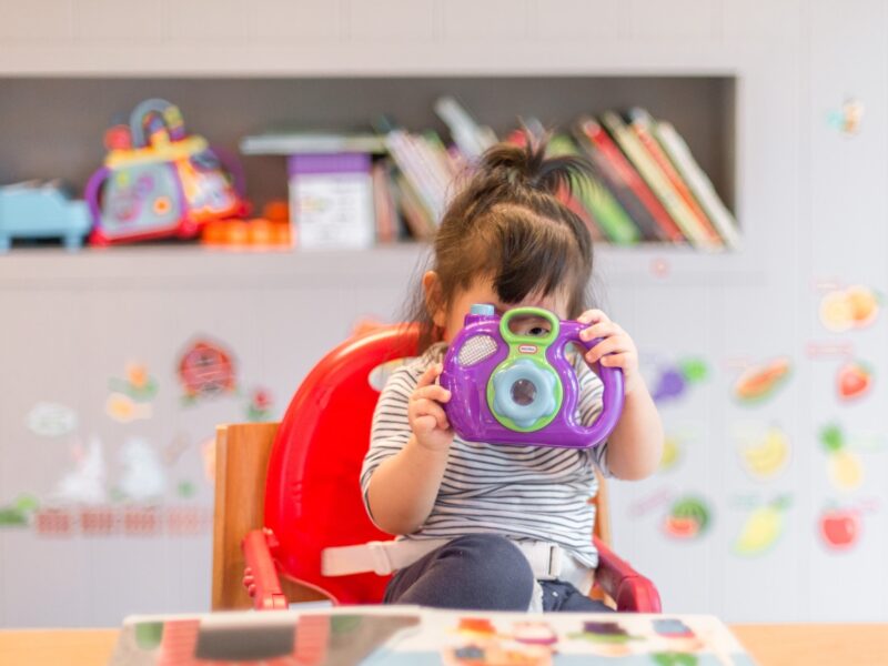 Toddler sat in a highchair and playing with a camera