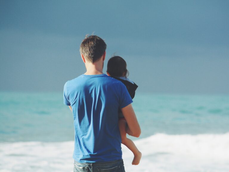 Dad on beach looking out to sea holding child