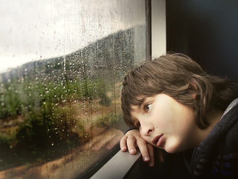 Bored child looking out of a train window in the rain