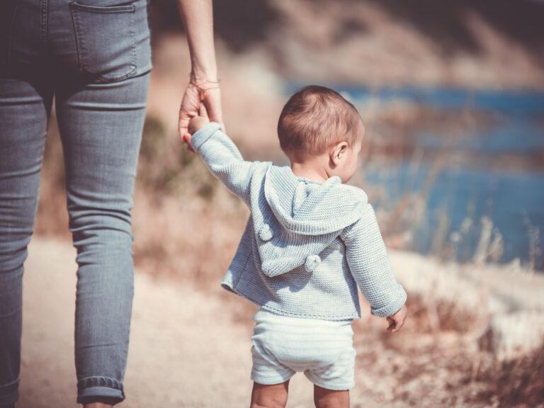 Toddler holding mum's hand whilst taking his first steps